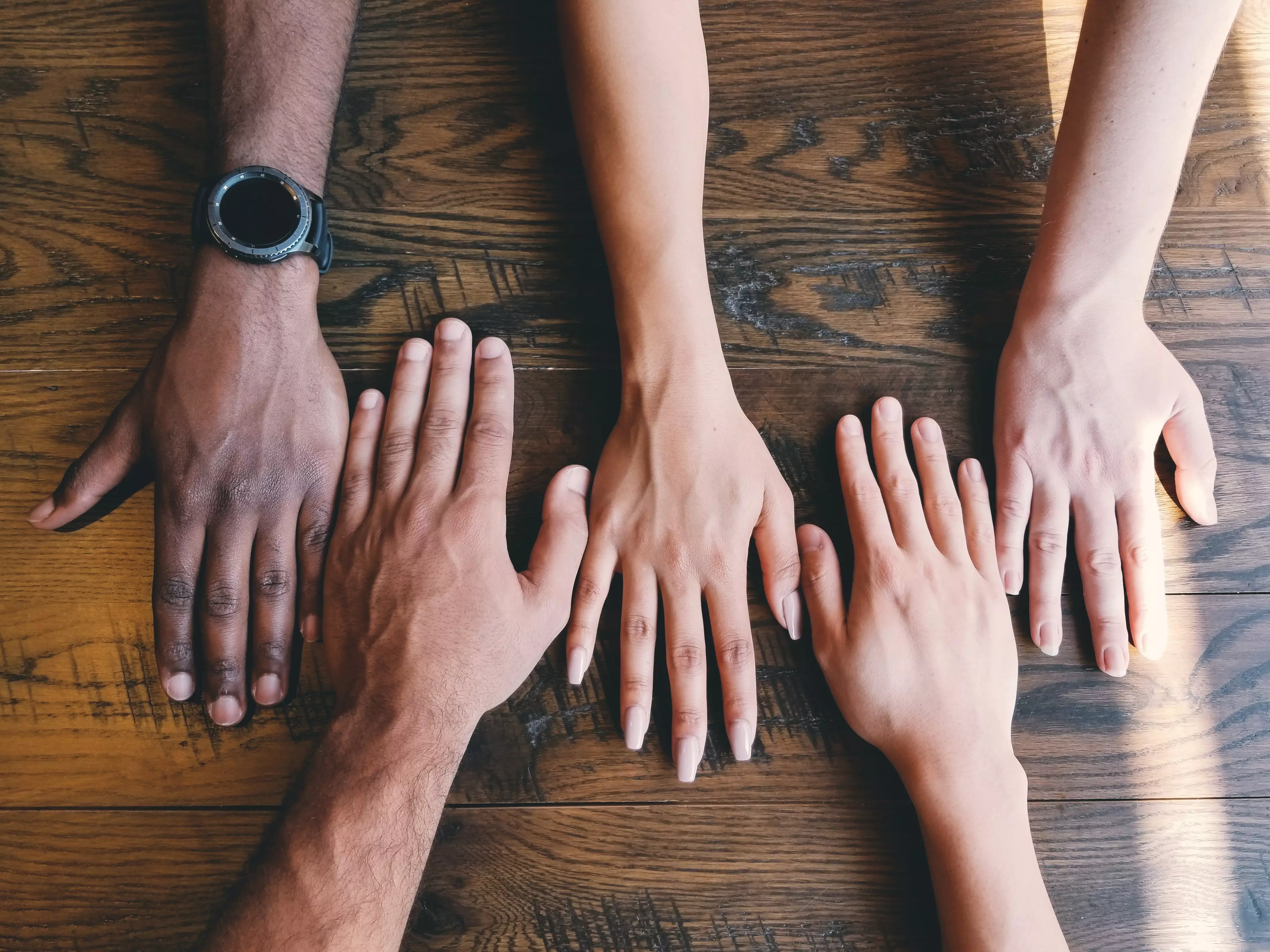 Colaboradores de diversas raças, com as mãos juntas, umas ao lado das outras.